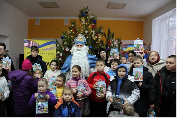 Святитель Миколай вітає дітей-переселенців, які тримають подарункові набори від партнерів фонду «Червона Калина Харків»